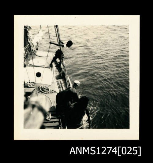 A person over the side of a boat, with a scuba diving helmet on, being lowered into the water with the assistance of a male, with a rope, on Packe Island