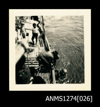 A person over the side of a boat, with a scuba diving helmet on, being lowered into the water with the assistance of a male, with a rope, on Packe Island