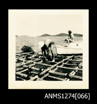 Two men on a pearl diving raft over the water, also with a boat, on Packe Island