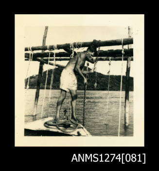 A man standing on the top of a boat, leaning on the wooden pearl raft next to him, on Packe Island