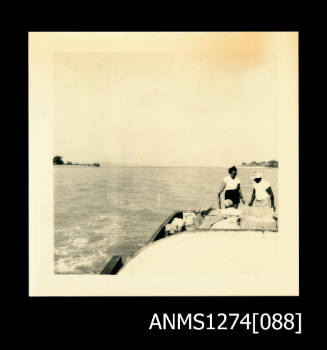 Three people sitting and standing in a boat, on Packe Island