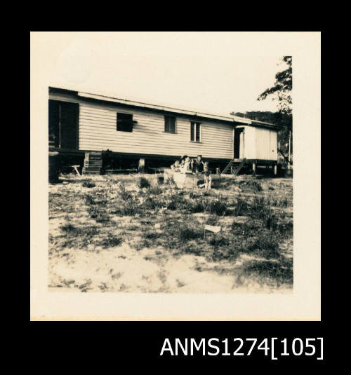 A house on sand, with people sitting in front of the house, on Packe Island