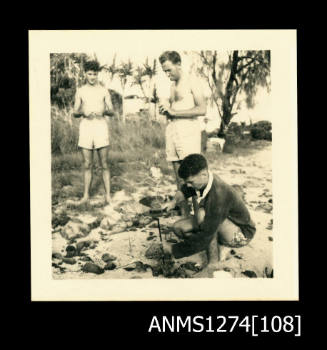 Three men opening pearl shells in sand on Packe Island