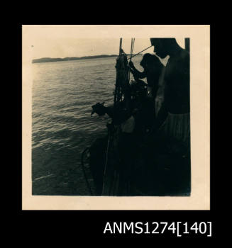 Photograph of several men looking over the side of a boat at the water at Packe Island