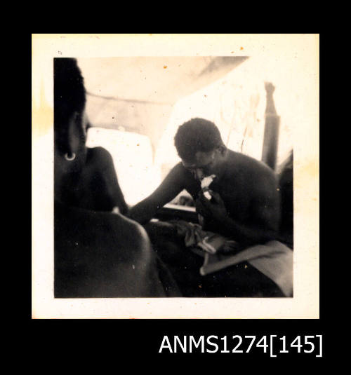 Two people, sitting under a shade cloth on a boat, on Packe Island