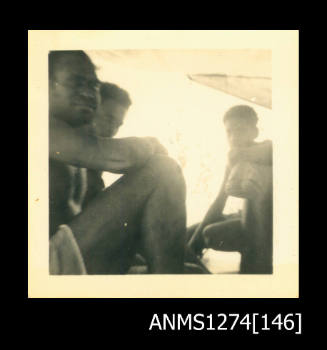 Three people, sitting under a shade cloth on a boat, on Packe Island