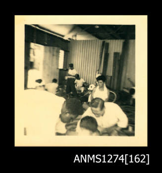 Photograph of numerous people sitting in a shed, on Packe Island