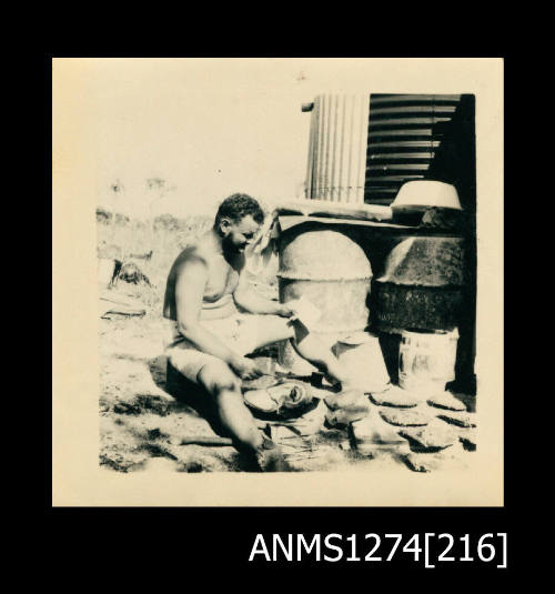 A man, possibly Denis George, sitting on the ground, with pearl shell laid out in front of him, on Packe Island