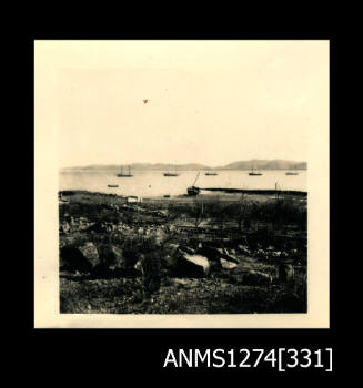 Photograph of equipment lying on land, and water in the background with several boats, on Thursday Island