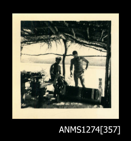 Two men (one is Denis George), standing under a shade structure on the beach, with various pieces of equipment, on Packe Island