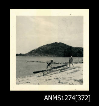 A two men standing on a beach (the man on the left is Denis George), with mangrove tree logs, on Packe Island