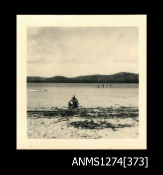 A man, crouching on a beach, de-barking a mangrove log on Packe Island