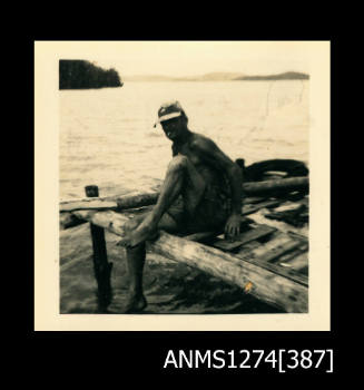 A man, sitting on top of a wooden structure, over the water, on Packe Island