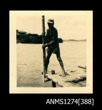 A man standing on a wooden structure over the water, holding a wooden pole, on Packe Island