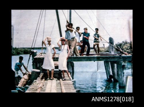 35mm colour transparency of men and women on a wharf; the two women are posing wearing white dresses, and the men are pulling on ropes