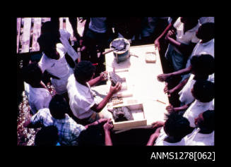 35mm colour transparency of numerous men standing around a table, with one man working on a pearl shell