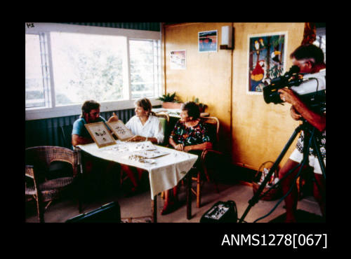 35mm colour transparency of three people sitting at a table with pearls on boards, being filmed by someone with a camera