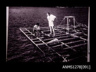 Two men standing on a wooden raft over the water