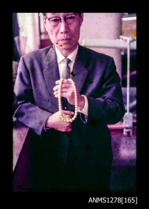 35mm colour transparency of a Japanese man holding a pearl necklace