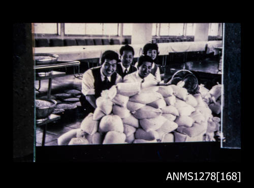 35mm colour transparency of four Japanese people standing behind a pile of white bags