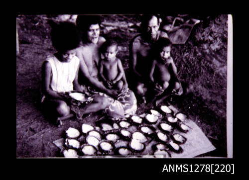 A male, female, and three children Papua New Guineans, sitting behind laid out rows of pearl shells