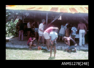 35mm colour transparency of numerous people congregated underneath a shed