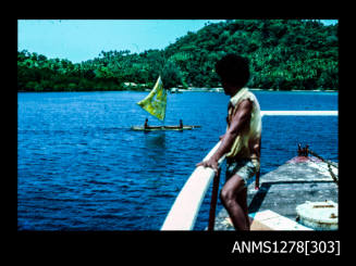 35mm colour transparency of a Papua New Guinean man standing on a boat, looking at a small sailing boat in the water