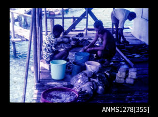 35mm colour transparency of three Papua New Guinean people, sitting on a verandah, possibly opening pearl shells