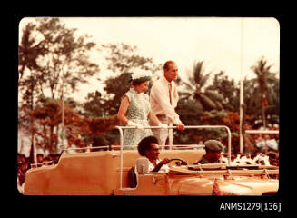 Queen Elizabeth II and Prince Philip standing in the open top of a car during their visit to Milne Bay