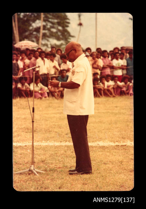 Man standing at a microphone making a speech during Queen Elizabeth II and Prince Philip's visit to Papua New Guinea in 1977