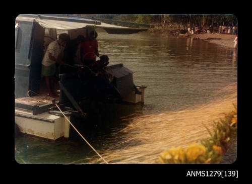 Four people in a boat, with one dressed in scuba diving gear, during Queen Elizabeth II and Prince Philip's visit to Papua New Guinea in 1977