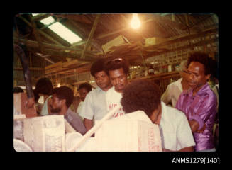 Papua New Guinean men standing in a shed, watching a demonstration during Queen Elizabeth II and Prince Philip's visit to Papua New Guinea in 1977