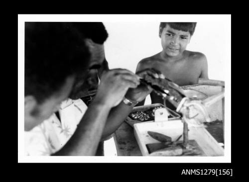 A Papua New Guinean man seeding a pearl shell, with a boy watching