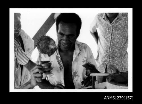 A Papua New Guinean man, looking at a pearl shell being held with pliers