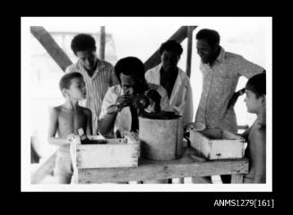 A Papua New Guinean man seeding a pearl shell at a desk, with three men and two boys looking on