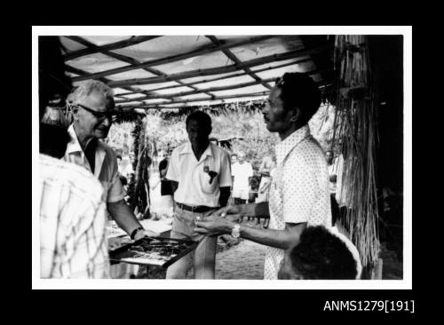 Two Papua New Guinean men and Denis George, who is holding out a tray in front of his body