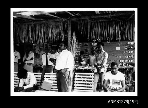 Photograph of several Papua New Guinean men standing or sitting in a room containing pearl and pearl shell displays on the walls and on a long desk