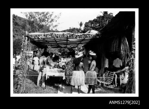 Papua new Guinean people, including two girls in traditional dress, viewing a pearl display underneath a tent