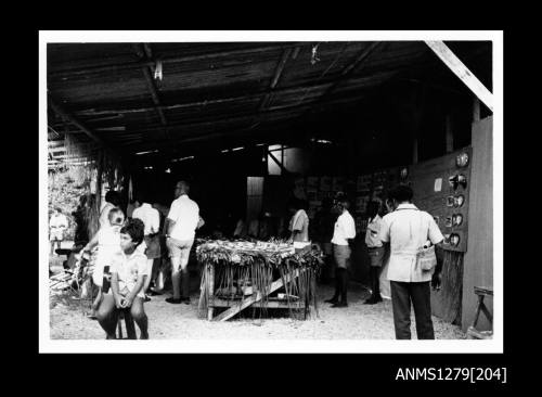 Photograph of several people standing in a shed, vieweing a pearl display on the walls and a large table in the centre of the room