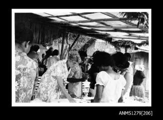 An elderly lady standing behind and several Papua New Guinean women looking at a table containing a pearling display