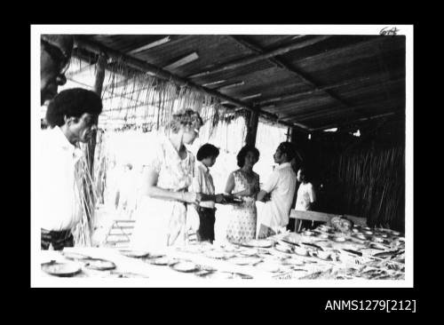 Photograph of several men and women, including Yurie (or Yulie) George and her son, standing beside a table displaying numerous pearl shells