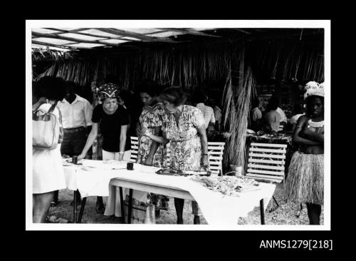 Photograph of several women, including one in traditional dress, looking at a table containing a pearl display