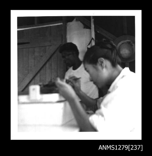 Yurie (or Yulie) George seeding a pearl shell, with a Papua new Guinean man standing in the background