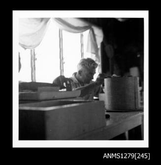 A man with grey hair sitting at a desk with pearling equipment, seeding a pearl shell