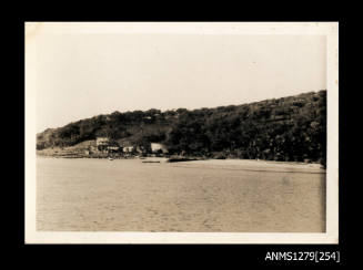 Photograph, taken from a boat, of shoreline, including buildings, beach and trees