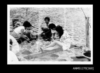 Photograph of several people sitting in a group, cleaning pearl shells