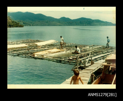 Colour photograph of three Papua New Guinean men standing or sitting on a wooden pearl production raft