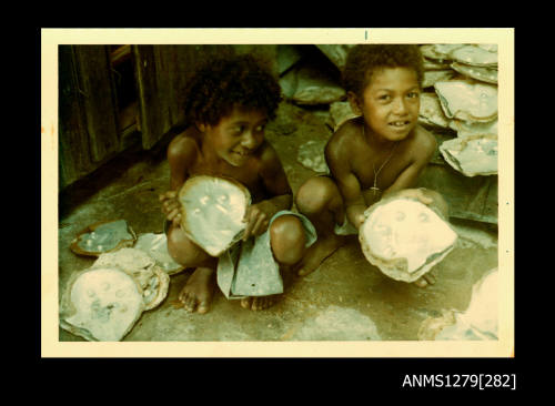 Colour photograph of two Papua New Guinean boys holding, and surrounded by, pearl shells with blister pearls