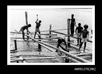 Photograph of several Papua New Guinean men constructing a pearl raft out of wood