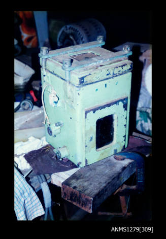 Colour photograph of a green painted, metal underwater camera case, sitting on a work bench